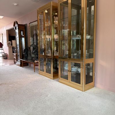 Pair of Hollywood Regency style brass and glass display cabinets, featuring interior lighting and glass shelving, circa 1970s.