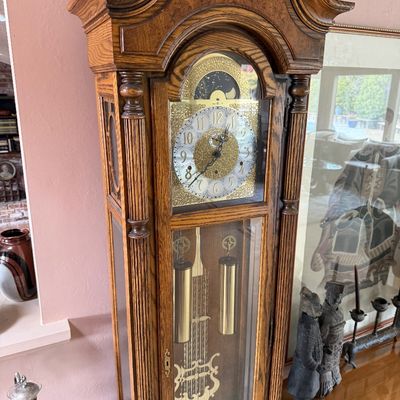 Vintage oak grandfather clock featuring an ornate bonnet top, fluted columns, and a brass dial with a moon phase indicator.