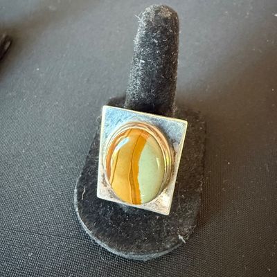 Vintage sterling silver ring featuring a large, oval picture jasper cabochon set on a square bezel, displayed on a black velvet ring stand.