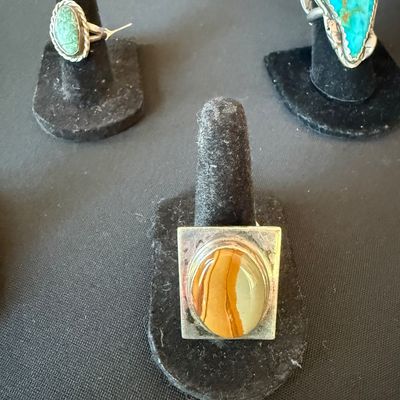 Three sterling silver rings featuring natural stone cabochons, including turquoise and picture jasper, displayed on black velvet ring...