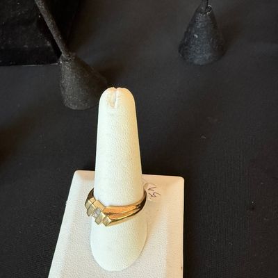 Gold band ring featuring a modern, asymmetrical design with small inset diamonds, displayed on a white cone stand.