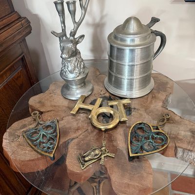 Assorted vintage metalware including a pewter stag-head candelabra, a lidded pewter stein, brass trivets, and a small crucifix, displayed...