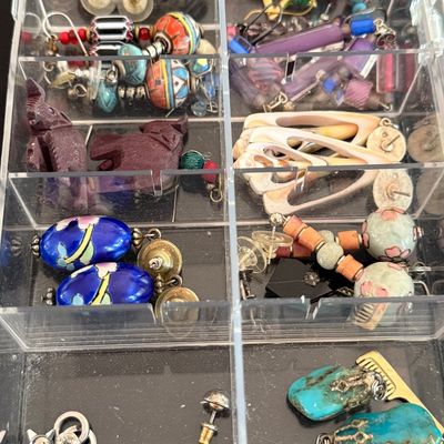 Assorted vintage costume jewelry, including beaded earrings, cloisonné pieces, and turquoise charms, organized in a clear plastic...