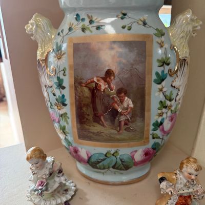 Vintage light blue porcelain vase featuring a hand-painted pastoral scene, floral accents, and lion head handles, accompanied by two...