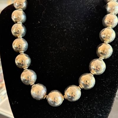Vintage sterling silver beaded necklace featuring large, polished spherical beads separated by small fluted spacers, displayed on a black...
