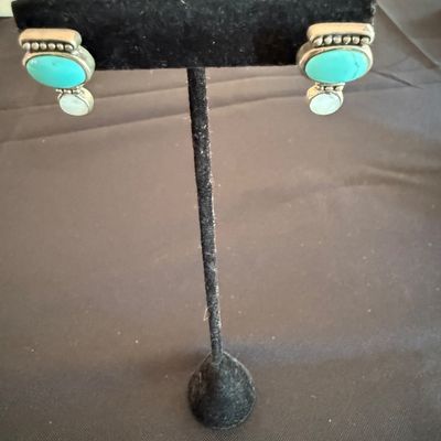 Pair of Southwestern-style sterling silver earrings featuring oval turquoise cabochons accented with smaller white stones, displayed on a...