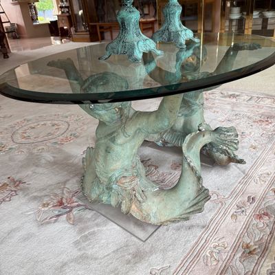 Neoclassical style coffee table featuring a thick oval glass top supported by two verdigris-patinated bronze merman or triton figures.