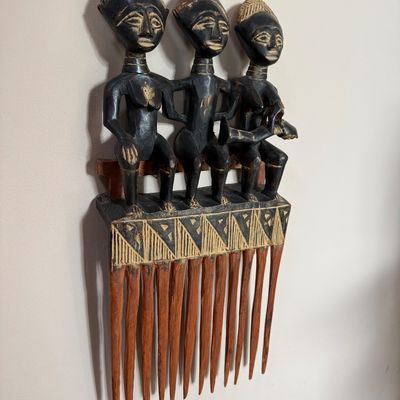 Hand-carved African wooden comb wall hanging, featuring three seated figures with geometric patterns and long tines.