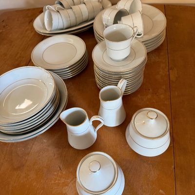 Vintage white porcelain dinnerware set with gold trim, including plates, bowls, teacups, saucers, creamers, and sugar bowls.