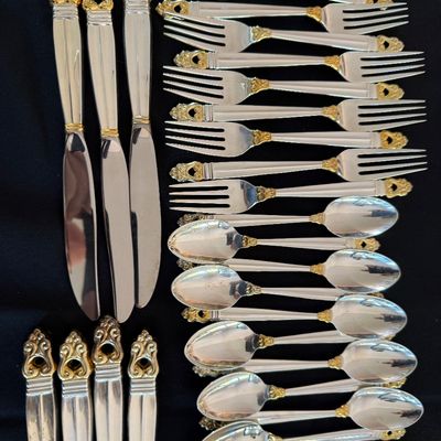 Vintage sterling silver flatware set with ornate gold-accented handles, including knives, forks, and spoons, showing minor wear from use.