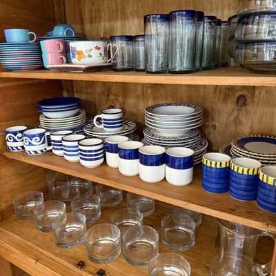 Assorted glassware and ceramic tableware, including blue-rimmed drinking glasses, striped mugs, and clear glass bowls, arranged on wooden...