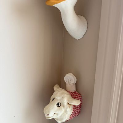 Whimsical wall-mounted animal heads, featuring a white goose with a yellow beak and a sheep wearing a red-and-white gingham collar and...