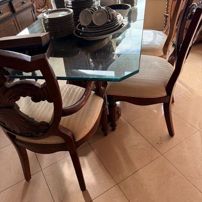 Traditional dining set featuring a glass-top table with carved wooden pedestals, accompanied by matching upholstered chairs with ornate...