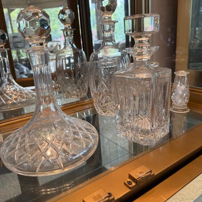 Collection of vintage cut crystal decanters with stoppers, displayed on a glass shelf inside a mirrored cabinet.
