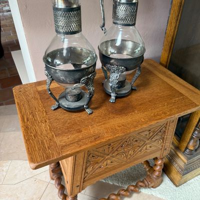 Pair of vintage silver-plated and glass coffee carafes with warming stands, displayed on a carved oak side table with barley twist legs.