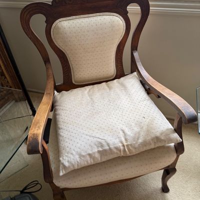 Antique carved wood armchair with cream-colored patterned upholstery, featuring a matching throw pillow and elegant cabriole legs.