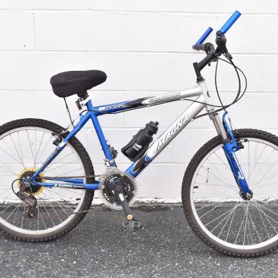 Magna Great Divide 21-speed mountain bike in silver and blue, featuring Shimano equipment, front suspension, and an attached water bottle...