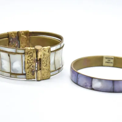 Two vintage brass bangles, including a wide hinged cuff with mother-of-pearl inlay and a slim purple-toned shell inlay bracelet marked...