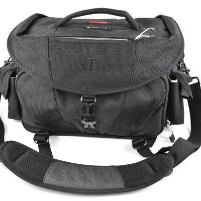 Tamrac black nylon camera shoulder bag featuring a padded strap, top carry handle, and multiple zippered compartments.
