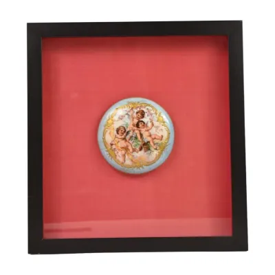 Vintage hand-painted porcelain plaque depicting cherubs, mounted on a red fabric background inside a black shadow box frame.