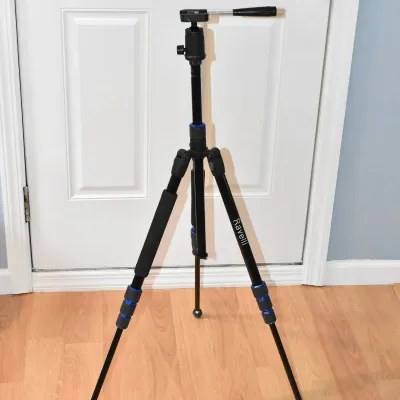 Ravelli black aluminum camera tripod with blue accents and a pan-tilt head, standing on a wood floor.