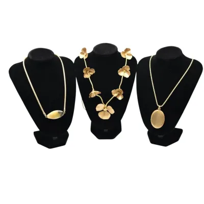 Three vintage gold-tone necklaces displayed on black velvet busts, featuring a modern slide pendant, a floral motif collar, and a classic...