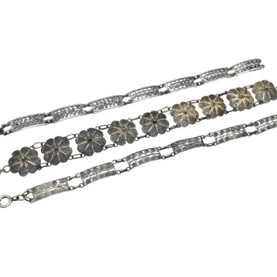 Three vintage silver filigree link bracelets, featuring intricate openwork panels and floral motifs.