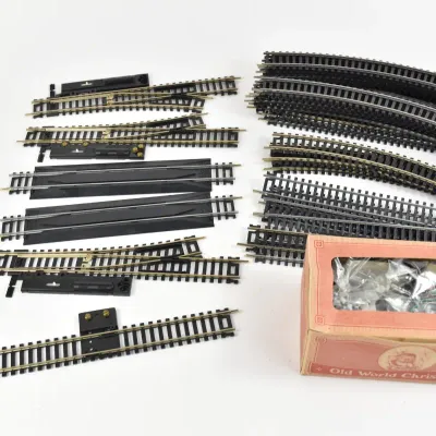 Assortment of HO scale model train tracks, including straight, curved, and switch track pieces, alongside an Old World Christmas box...