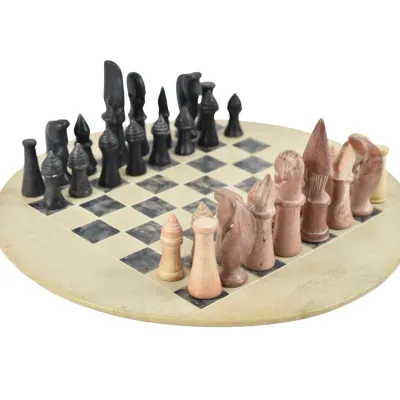 Hand-carved soapstone chess set featuring a circular board and stylized, abstract playing pieces in black and pinkish-tan tones.