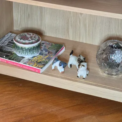 Assorted decorative items on a wooden shelf, including a floral ceramic trinket box, three miniature cat figurines, and a cut-glass rose...