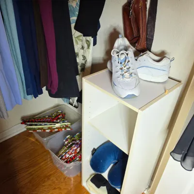 White laminate three-shelf bookcase holding a pair of white athletic sneakers and a blue neck pillow, shown inside a closet.