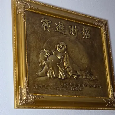 Framed Chinese relief plaque depicting a laughing Buddha with gold-toned finish and ornate frame.