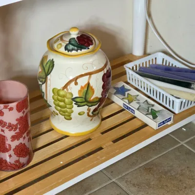 Ceramic lidded jar with hand-painted grape motif, displayed alongside a pink floral glass candle holder and assorted taper candles on a...