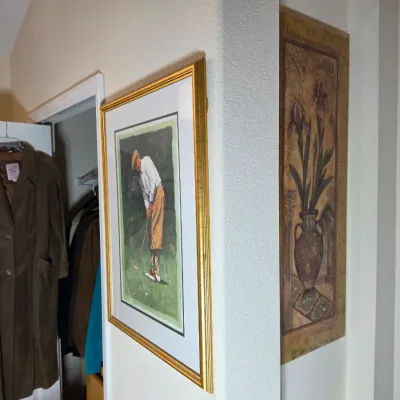 Framed vintage-style golf print in a gold-finished frame, alongside a long brown suede trench coat hanging on a door.
