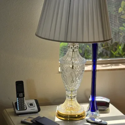 Vintage cut glass table lamp with a brass base and pleated white shade, shown alongside a cobalt blue glass bud vase on a nightstand.