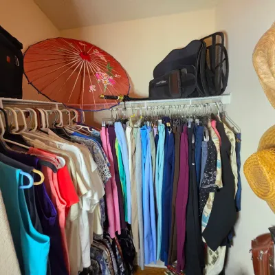 Closet filled with various clothing items, including colorful shirts and pants, alongside accessories like straw hats, a red parasol, and...