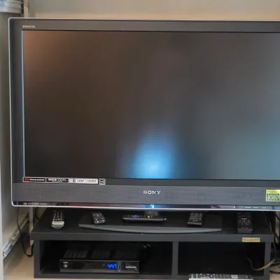 Sony Bravia Full HD 1080 television set on a black media stand with multiple remote controls and a Technicolor receiver.