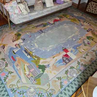 Large hook-style area rug featuring a coastal landscape design with lighthouses, sailboats, and windmills, bordered by seashells and...