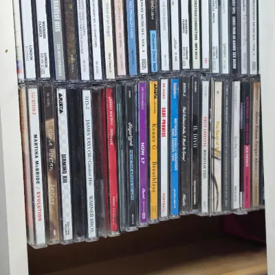 A collection of music CDs in jewel cases, featuring classical, pop, and country artists, organized on a white shelf.