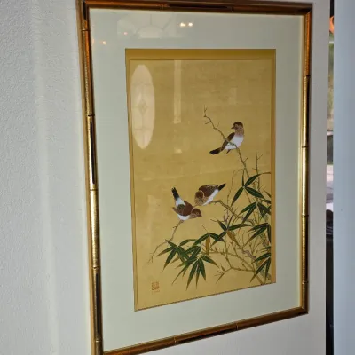 Framed Asian-style silk painting depicting three birds perched on bamboo branches, housed in a gold-finished faux bamboo frame with a...