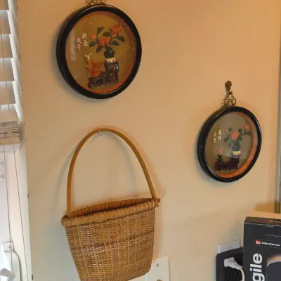 Pair of vintage Chinese shadow box wall hangings with carved stone floral motifs, displayed alongside a woven wicker wall basket.