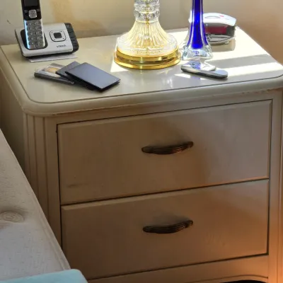 Postmodern two-drawer nightstand in a light laminate finish with curved edges and dark metal pulls, showing some wear along the top edge.