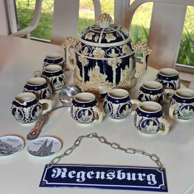 Vintage German Regensburg punch bowl set featuring a large lidded tureen, matching mugs, a metal ladle, and a decorative hanging sign.