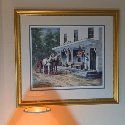 Framed and matted print depicting a horse-drawn carriage in front of a historic general store, housed in an ornate gold-finished frame.