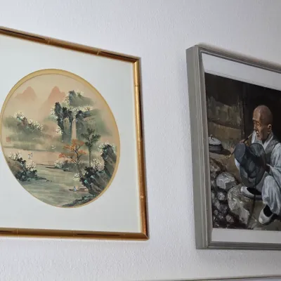 Two framed Asian-style artworks, including a circular landscape painting in a gold faux-bamboo frame and an oil painting depicting an...