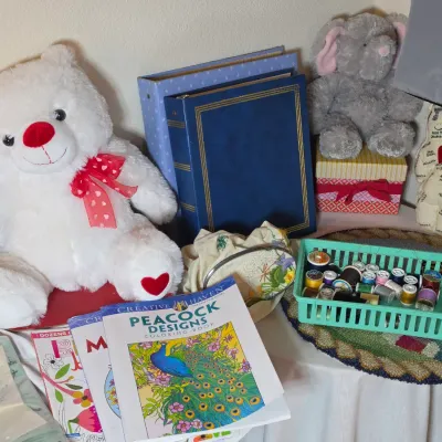 Assorted craft supplies and plush toys, including coloring books, a basket of sewing thread spools, photo albums, a white teddy bear, and...
