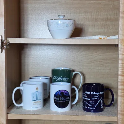 Assorted ceramic coffee mugs with various promotional and inspirational prints, displayed alongside a lidded porcelain sugar bowl on...