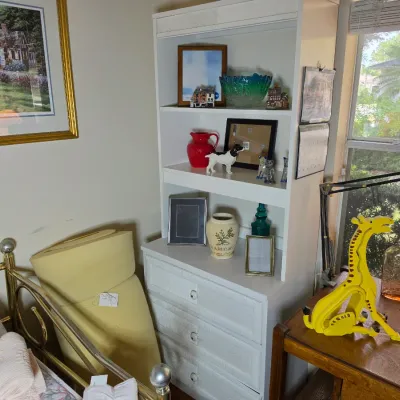White wicker-front three-drawer chest with an attached hutch bookcase, displaying various decorative items, picture frames, and glassware.