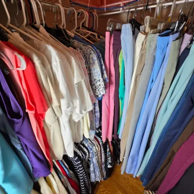 Assorted women's clothing, including colorful tops, blouses, and trousers, hanging organized in a closet.