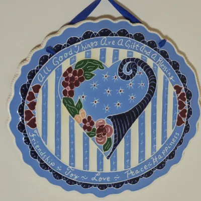 Hand-painted ceramic wall plaque featuring a blue and white striped background, a central heart with floral details, and inspirational...